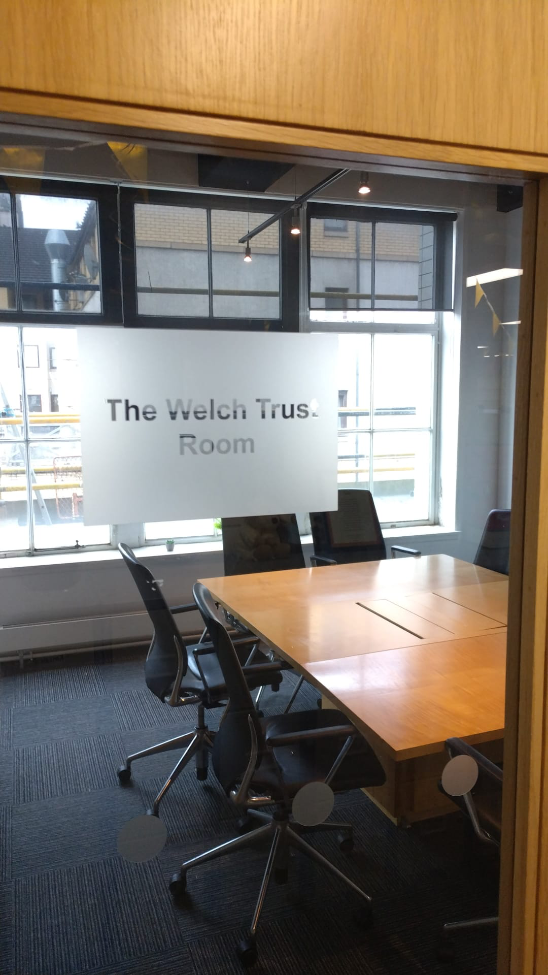A glass meeting room door etched with the words The Welch Trust Room, a boardroom table and chairs inside