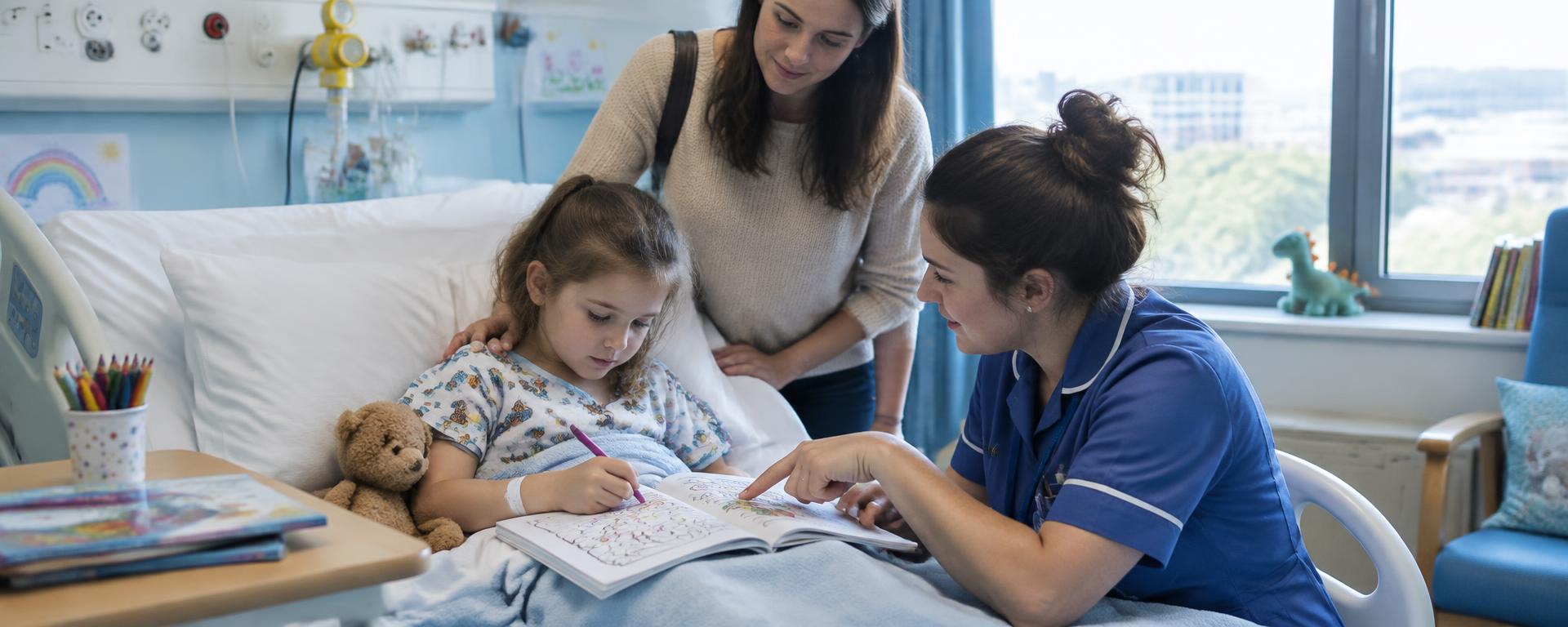 A children's nurse helping a young patient with her schoolwork at her hospital bed, her mother beside them on a bright children's ward